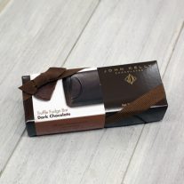 A rectangular, dark brown box with a white dark chocolate sleeve on it. The box has a brown ribbon on it.