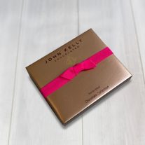 A Closed 6 piece assortment box with a fuchsia ribbon. The lid is a satin gold and features the logo John Kelly Chocolates