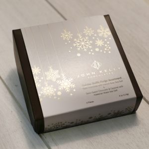 A dark brown box with a white sleeve. The white sleeve has elegant gold snowflakes on it. In the bottom right corner of the white sleeve is a John Kelly Chocolates logo and the product name.