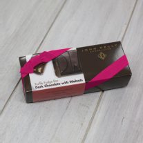 A dark chocolate with walnuts 8oz bar box with a fuchsia ribbon. The box is brown and has a label on it with an image of the DW on the dark chocolate with walnuts bar.